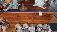 Front view of the wooden cedar lined trunk chest with visible wood grain, showing several vintage dolls placed on and around it.