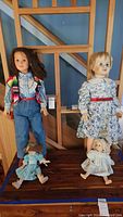 Four vintage dolls on wooden surface: two large standing dolls and two smaller seated dolls