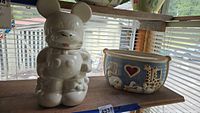 Photo showing both Mickey Mouse and Noah's Ark ceramic cookie jars on a wooden shelf under a window with blinds.