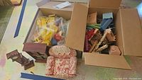 Box containing multiple small dollhouse furniture pieces, some in plastic packaging.