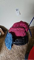 Lot of four bags including two pink Lug bags, one black Lug bag, and a blue paisley patterned bag on carpeted floor