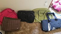 Five Lug brand bags side by side: pink quilted, brown quilted, black briefcase style, light green rounded, navy blue quilted tote with 'love' text