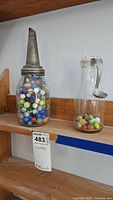 Wide shot showing vintage glass jar with metal spout lid filled with colorful marbles, and milk bottle with marbles and cream ladle