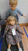 Photo showing both boy and girl My Twin dolls seated on floor, girl doll in floral dress and boy doll in striped shirt and glasses.