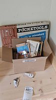 Box containing original Pocketools packaging and instruction manuals with miniature tools visible inside.