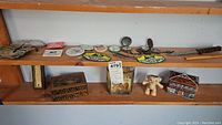 Shelf view displaying pocket watches, various collectible tins, keepsake box, teddy bear figurine, and a house-shaped tin.