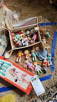 Overview of the toy collection with Cabbage Patch Kids dolls and other small figures in storage bins on carpet.