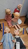 Group photo of five vintage Whimsie dolls seated on a wooden floor showing their varying clothing and missing hair.