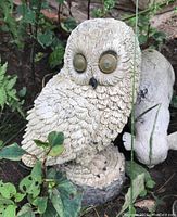 Close-up photo of a detailed resin owl garden sculpture on natural ground surrounded by foliage.