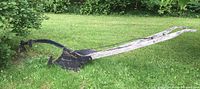 Side view of antique single furrow plow on grass, showing long wooden handles and metal furrow blade with hitch.