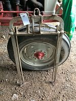 Front view of cast iron bale lifter standing in front of a tractor tire, showing the lifting prongs, frame, and hook eye.