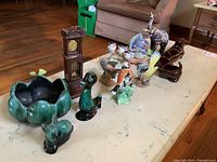Wide angle photo of the full collection of pottery bird and animal figurines alongside a wooden clock figurine on a table