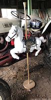 Front and side view of white resin carousel horse with black saddle and gold detailing, mounted on gold pole with round base, showing wear and minor damage