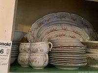 Photo showing stack of teacups and matching saucers, front view showing floral pattern and gold rims