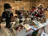 Wide view of the Christmas decoration lot on a table, showing various snowmen, Santa figures, snow globes, and some boxed ornaments.