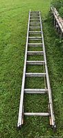 Full length view of the 26-foot aluminum extension ladder laid on grass, showing weathered condition.