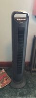 Full view of black Seville Classics tower fan standing on carpet near wall, showing front grill and base.