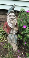 Full view of garden gnome partially surrounded by plants showing overall condition and size.