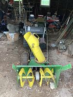 Front view of John Deere snowblower showing two large yellow augers and green housing, chute for snow discharge is bright yellow.