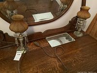Full view of both vintage crystal and glass lamps with amber-colored glass shades on either side of an oval wooden framed mirror on wooden furniture.