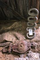 Photo showing multiple weathered lead grips stacked and a rusted large metal pulley block on a textured surface.