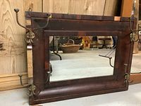 Front view of rectangular mirror with dark wooden frame and metal coat hooks on sides, showing scratches and wear.