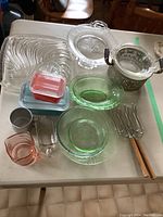 Overview of all items on table showing Pyrex fridge boxes, green and pink glass pieces, clear glass serving plates, metal warming dish, and serving forks.
