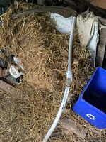Full view of the vintage scythe lying on hay with aluminum handle and curved rusty blade, showing weathered condition.