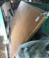 Four stacked 1/4 inch mahogany plywood sheets leaning against a garage wall with some surrounding tools and materials visible.