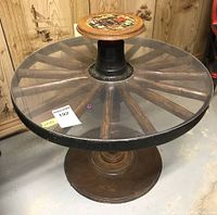 Full side view of the wagon wheel pedestal side table showing the wooden spokes base and glass top.