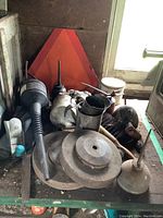 Multiple vintage oil cans, metal funnels, a black flexible spout oil can, a red reflective emergency safety triangle, and some miscellaneous hardware parts positioned on a table in a garage.