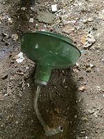 Green enamelware lamp resting on dirt ground, showing body and wiring.