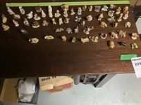 Overview photo showing 55 Wade ceramic figurines arranged in rows on a wooden table including various characters, animals, and small houses.