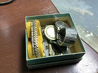 Lot of watches inside a green box with yellow padding showing metal link watch bands and watch faces.