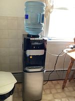 Full view of the Chef water dispenser showing large water bottle, dispenser spout area, stainless steel lower cabinet, and the surrounding environment.