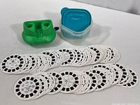 Set of over 30 circular Viewmaster slide reels laid out, some stacked, next to a blue plastic container