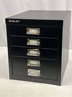 Full view of closed black metal Bisley 5-drawer cabinet with labels on each drawer.