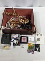 Mixed lot of costume jewelry including multiple necklaces, bracelets, earrings, and a silver ring placed beside a wood box not included in the sale.