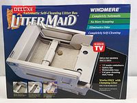 Front packaging showing the product name, image of the automatic litter box, and features including 12 waste containers, safety bar, removable tray, and cat paw cleaning mat/ramp.
