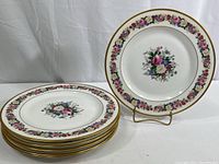 Six Limoges china dinner plates stacked, one displayed on stand showing full floral and gold rim design.
