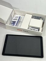 TCL TAB 8 LE tablet resting on white surface with open box showing accessories inside the packaging.
