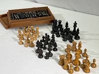 Four sets of 16 chess pieces each arranged by color with a wooden box containing black dominoes on the side.