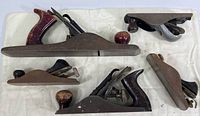 Top view showing all five vintage hand wood planers laid out on white fabric, showing size and shapes with wood and metal handles.