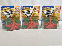 Three Hot Wheels Monster Jam sealed Surprise Truck packages featuring green gift box design with red bow, front view.
