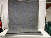 Full view of the large gray wool blanket hanging, showing three faint blue vertical stripes.