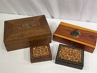Four wooden boxes together showing variety in size, wood type and decorative styles including floral inlay, painted sailboat, and marquetry.