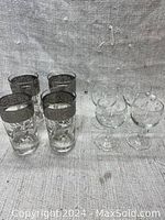 Both sets of glassware shown side by side, four high ball glasses and four small etched wine glasses.