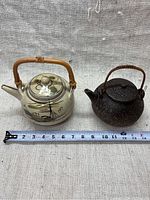 Two antique Asian teapots side by side with measuring tape for size reference.