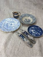 Overview of porcelain set showing 1 large plate, 1 shallow bowl, 1 small round dish, 1 creamer jug, and 2 crackled glaze ceramic rests shaped like animals with blue decoration on a beige fabric background