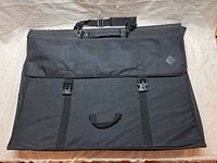 Full front view of the large black art portfolio showing carry handle and dual buckle closures.